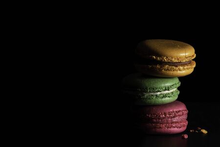 Colorful macaroons on dark black background. Variety of french almond macaron cookies in pile. Dessert, sugar, bakery creative concept. Macro shot, side view, close up, copy space. Low keyの写真素材
