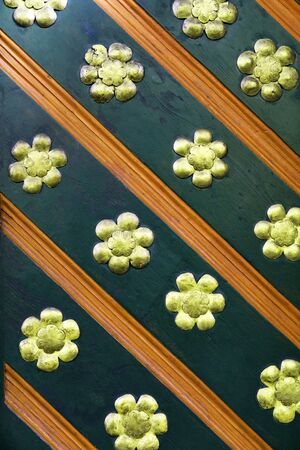 Old medieval wooden door detail. Abstract pattern wooden texture background. Diagonal stripes with flower details. Orange, green and golden details. Vertical, close upの写真素材