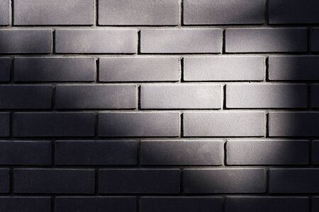 Black brick wall with sunbeam texture background. Beautiful new dark bricks with natural vignette. Modern building wall material. Close up, copy spaceの写真素材