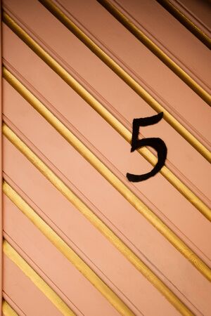 Old medieval wooden door detail with house number in sunlight. Pink and beige wooden door with golden pattern and number five. Abstract pattern wooden texture background. Close up, copy spaceの写真素材
