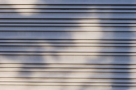 Silver metal wall texture background. Wall with beautiful pattern of different lines in sunlight with shadows and tree shades. Modern building wall from metal plates. Close up, copy spaceの写真素材