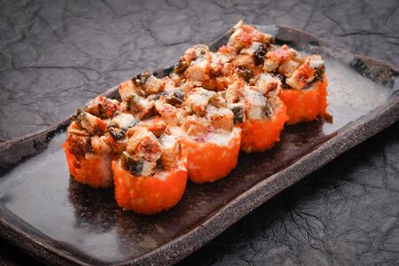 Sushi set served on black plate on dark background. Baked maki roll with eel, masago, salmon, cream cheese, avocado and prawn. Assorted sushi. Japanese food. Restaurant menu. Side view, close upの写真素材