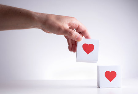 One female hand brings a white box with a red heart to another red box with a red heart on a white background, close up.の写真素材
