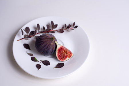 Two figs on a white plate with a branch of barberry  on the white table.の写真素材