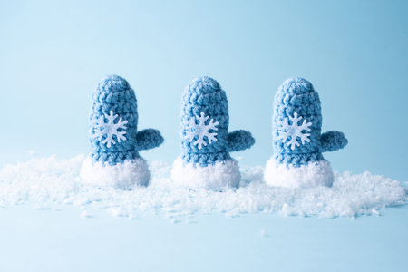 Three knitted blue mittens in the snow on a blue background, closeup.