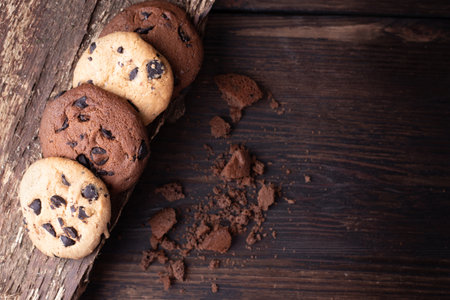 Four chocolate chip cookies and crumbs on a dark wooden background, top view, close up, copy space.の写真素材