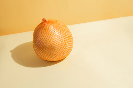 Yellow fresh pomelo in mesh packaging on a yellow and orange background in the sunlight, close up. Modern isometric concept.の写真素材