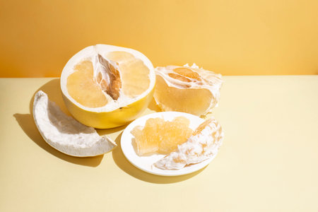 Fresh juicy pomelo half, wedges, pulp, and rind on a yellow background in sunlight, close up. Modern...