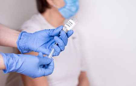 Gloved hands drawing covid-19 vaccine into a syringe from a vial. Vaccination of an elderly woman,...