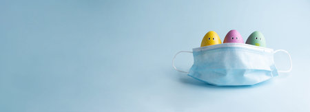 Three colorful easter eggs looking out of a medical mask, banner, copy space. Easter covid-19 concept.の写真素材