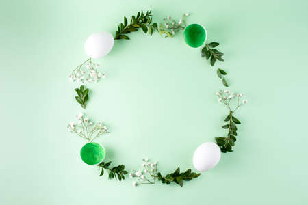 Easter frame made of eggs, flowers and green twigs on a green background, top view, flat lay, close up. Easter background.の写真素材