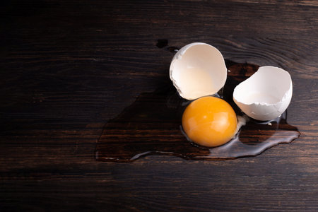 Broken chicken egg, yolk and egg white with shells on the dark wooden background, rustic style,...