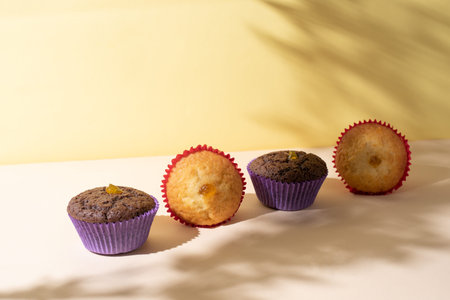 Row of chocolate and vanilla muffins on yellow background in sunlight with beautiful shadows, ckose...