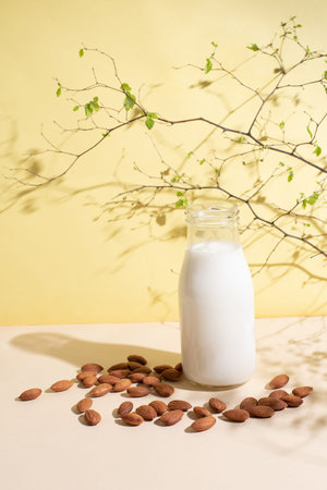Bottle with almond milk and almonds on a yellow background in sunlight, vegetarian milk, healthy...