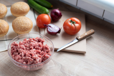 Ground beef in a glass bowl on the kitchen table with other hamburger ingredients, cooking at home, close up.の写真素材
