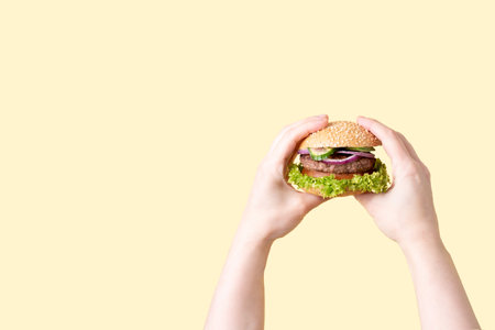 Two female hands holding delicious beef burger on the yellow background, close up.の写真素材