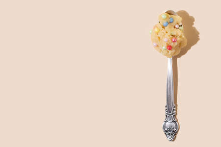 A spoon with edible cookie dough with colorful balls on a yellow background in bright light, close up.の写真素材