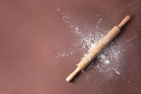 Wooden rolling pin in wheat flour on a brown background, close up.の写真素材
