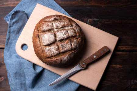 Large loaf of round rye bread on a cutting board with a knife on a wooden background, sitl rustic, close up.の写真素材