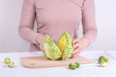 Female hands cutting into halves the head of a early cabbage on a white background, close up.の写真素材