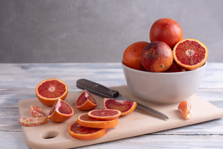 Sliced blood oranges on a cutting board with a bowl of citrus fruits on a gray background, close up.