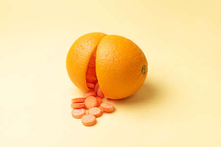 Falling out vitamin C tablets from two halves of orange peel, on a yellow background, vitamin C pills as an alternative to citrus fruits close up.の写真素材
