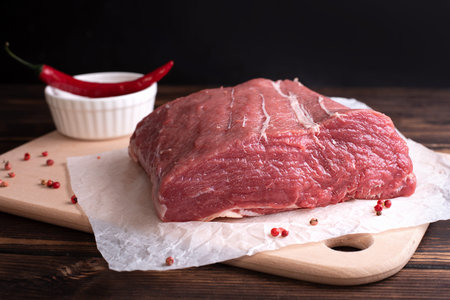 Raw meat on a cutting board, one large pieces of veal fillet on a dark wooden background, rustic...