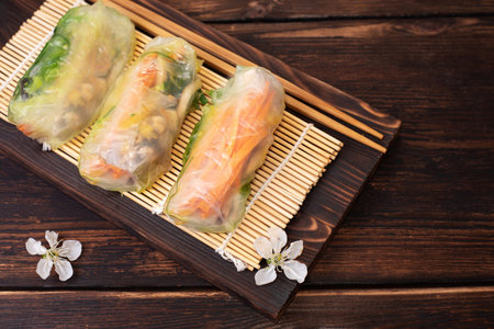 Fresh three spring rolls with cherry flowers on wooden board, vietnamese, asian food, close up.