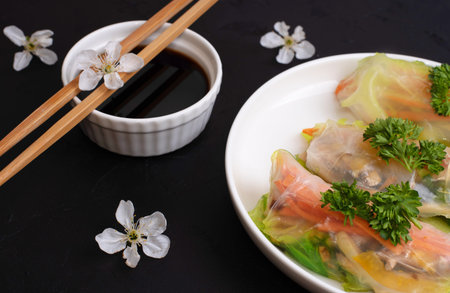 Soy sauce with spring rolls on a white plate with cherry flowers on black background, asian cuisine,...