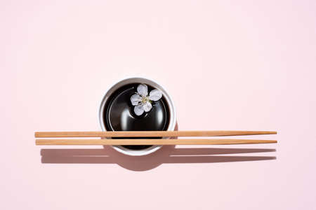 Soy sauce, teriyaki in white bowl with chopsticks and cherry blossom on pink background in bright sunlight, close up.の写真素材