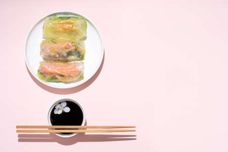 Asian cuisine, spring rolls on a white plate with cherry flowers and chopsticks on a pink background, close up.の写真素材
