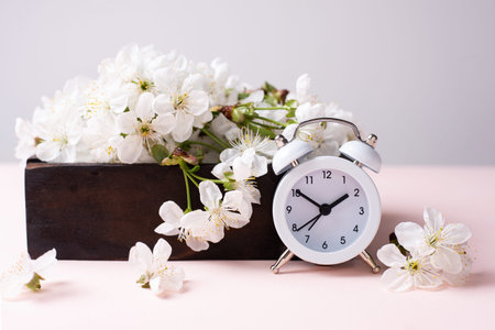 White vintage clock with wooden box with cherry flowers on pink background, spring time concept,...