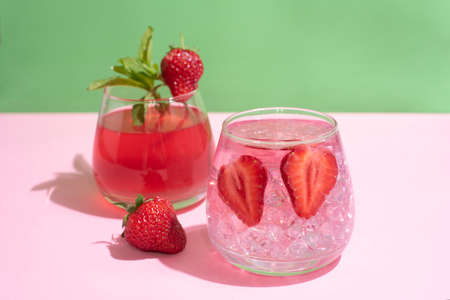 Glasses with functional water, strawberry lemonade with ice cubes on green and pink background, summer drinks concept, close up.の写真素材