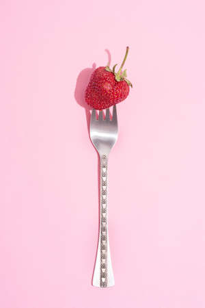 Fork with ripe strawberries on a pink background with a beautiful shadow, summer concept, close up.の写真素材
