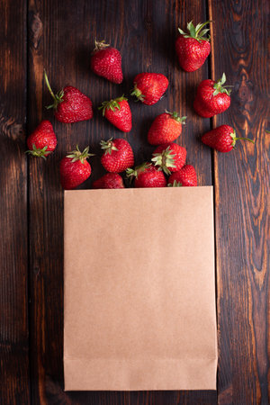 Paper bag with fresh strawberries on a wooden background, summer berries spilling out of the bag, close up.の写真素材
