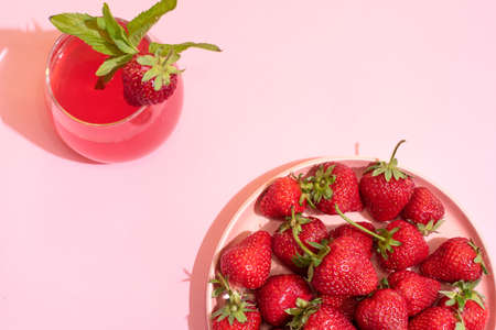 Plate with ripe strawberries and glass of strawberry lemonade on pink background, top view, summer concept, close up.の写真素材