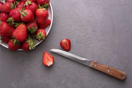 Plate with ripe strawberries and knife on gray concrete background, summer concept, close up.の写真素材
