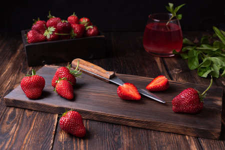 Juicy fresh strawberries on a cutting board with a knife on a dark wooden background, summer berries, healthy vegan food concept, close up.の写真素材