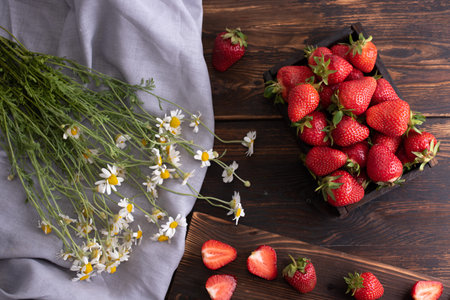 Box with ripe strawberries on a wooden background with a bouquet of daisies and textiles, summer concept, close up.の写真素材