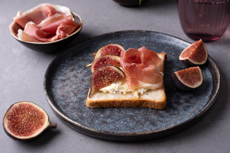 Crostini with Italian ham and ricotta, toast with prosciutto and figs on a dark background, close-up.の写真素材