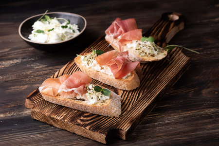 Toast with prosciutto ricotta and microgreens, ham crostini on a dark wooden background, rustic style.の写真素材