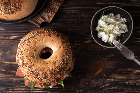 Cutting board with ham and ricotta bagels on a dark wooden background, prosciutto and cheese sandwich, rustic style.の写真素材