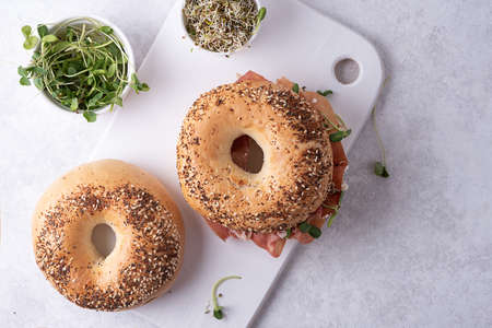 Two bagels and a bowl with microgreens on a cutting board, buns on a white background, top view.の写真素材