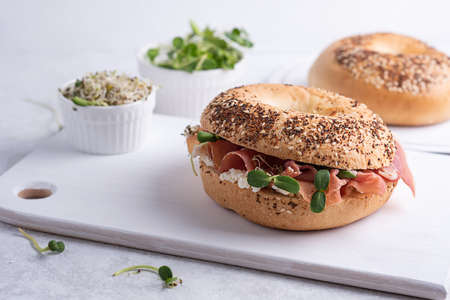 Tasty sandwich with prosciutto cheese and microgreens for breakfast, cutting board with ham and ricotta bagels on a white background, close-up.の写真素材