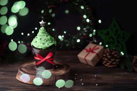 Christmas cupcake in the shape of a Christmas tree with bokeh lights and gifts, muffin with festive decor.の写真素材