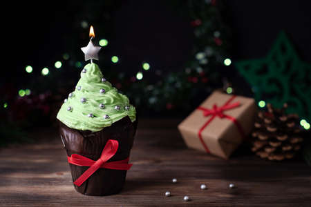 Christmas tree-shaped cupcake with a star candle and gifts on a dark wooden background, a muffin for Christmas.の写真素材
