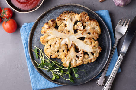Cauliflower steak on a plate with cutlery, healthy vegetarian lunch on gray background.の写真素材