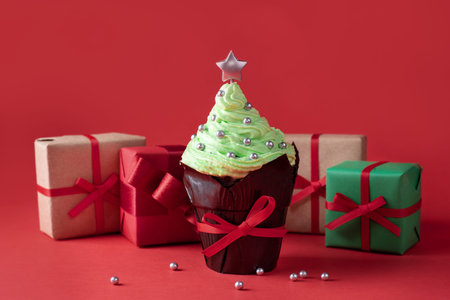 Cupcake with cream top in the shape of a christmas tree with gifts on a red background, christmas...