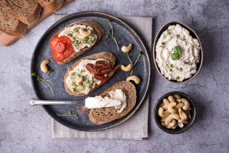 Bowl with fermented nut spread, sliced bread with cashew cream cheese, tomatoes and microgreens on a gray background.の写真素材