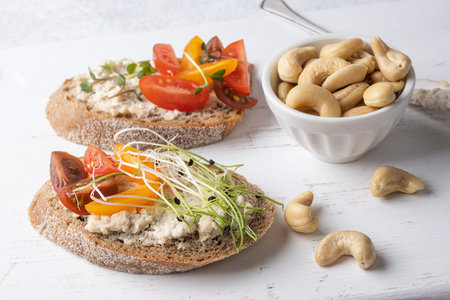 Sliced bread with cashew cheese, microgreens and tomatoes on white background, healthy snack made...